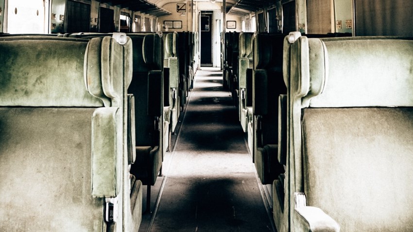 Empty old train interior with worn green seats in rows.